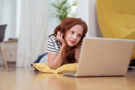 Pretty Young Woman Watching Movie on Laptop Computer Seriously While Lying on the Floor at the Home Living Room.