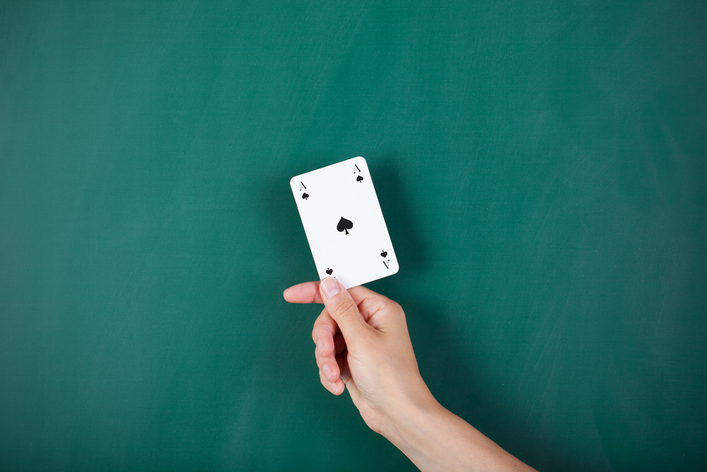 Closeup of womans hand holding ace card against green board