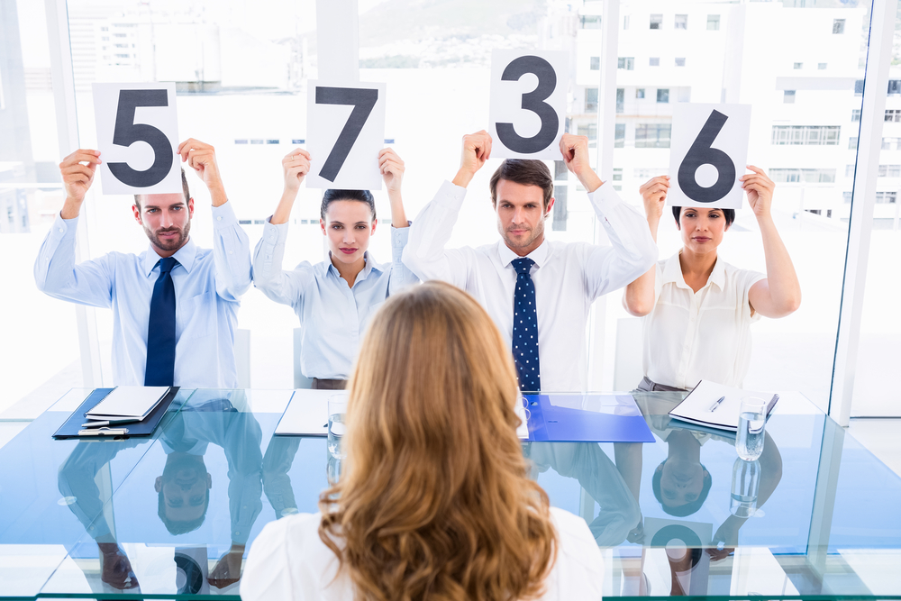 Group of panel judges holding score signs in front of a woman at bright office