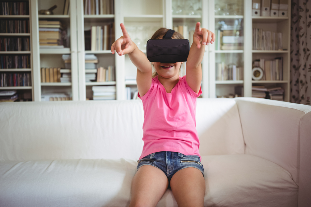 Happy girl looking through virtual reality headset in living room at home