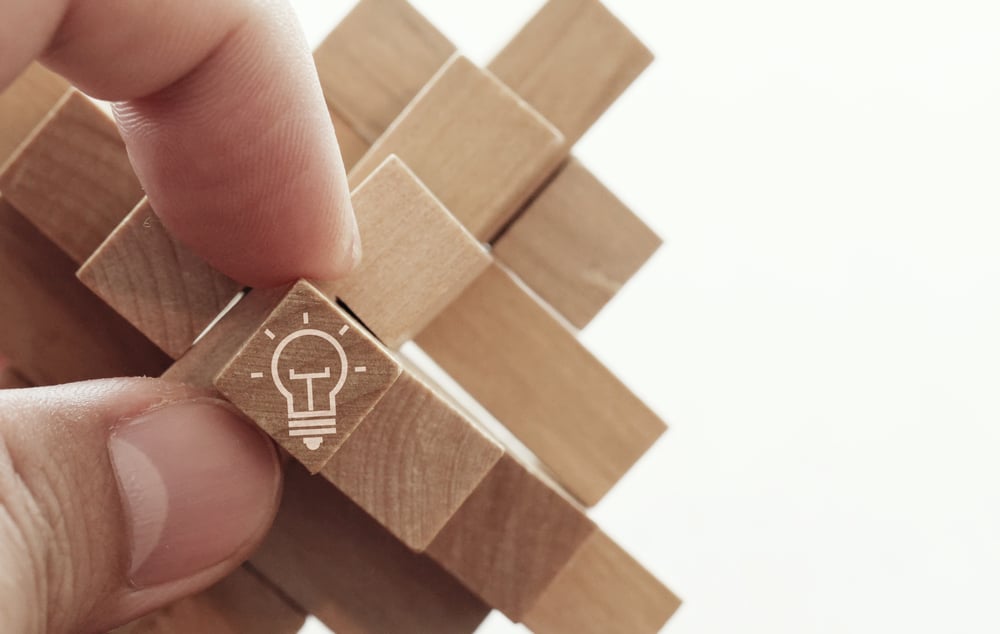 close up of hand showing illuminated light bulb icon on a wooden block puzzle as innovation concept